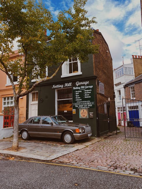 A two-storey brick building with a black painted ground floor, labeled 'Notting Hill Garage' and 'Notting Hill Garage' with white lettering and a list of services, situated on a cobblestone street in