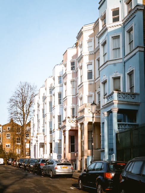 A row of multi-storey Victorian terraced houses with intricate white decorative mouldings and large bay windows, painted in pastel shades including pale pink, blue, peach, and cream. Each building fea